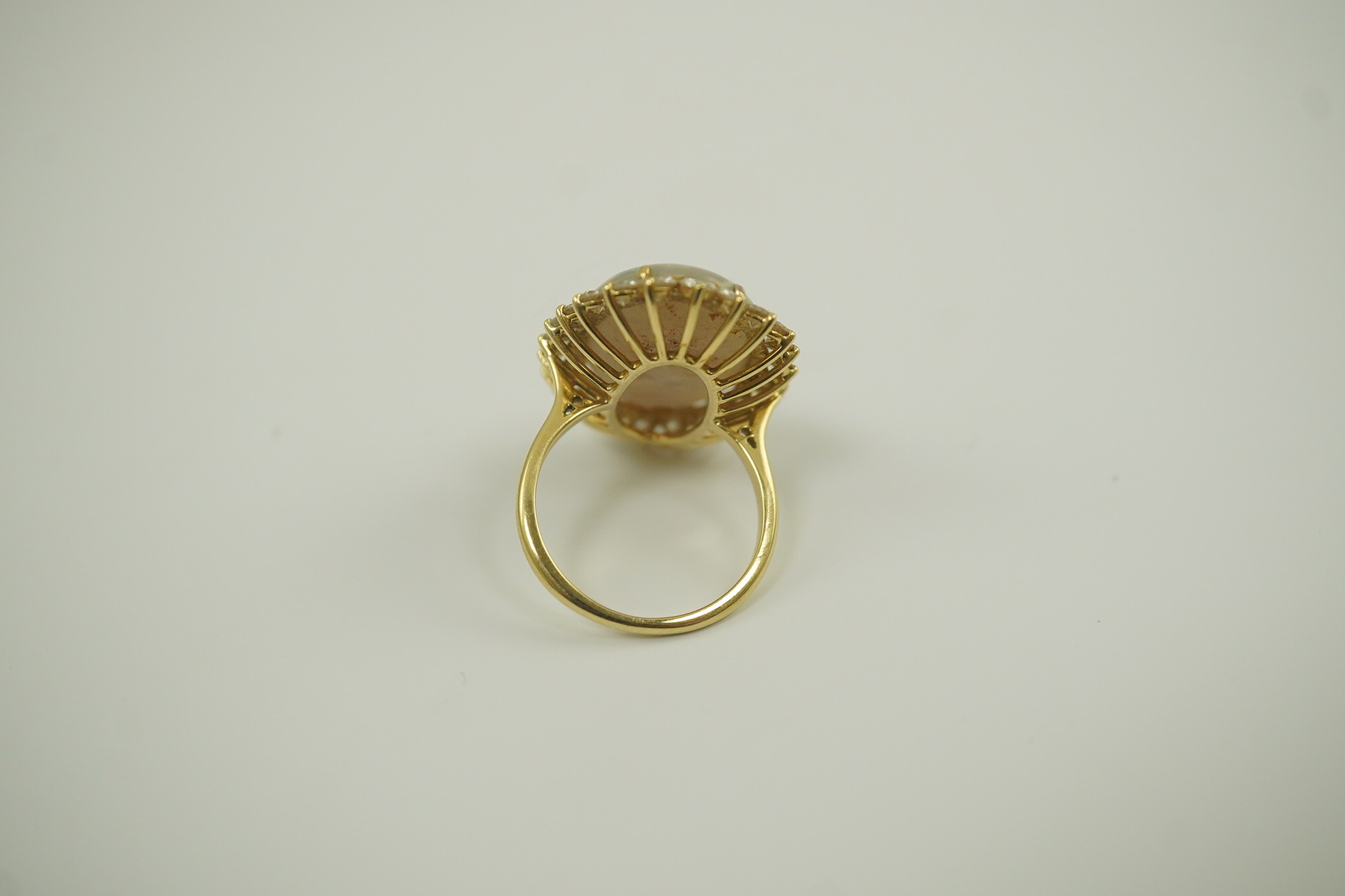 An 18ct gold, white opal and diamond set oval cluster dress ring, the cabochon opal measuring approximately 22mm by 14.5mm, with a depth of 5mm, and bordered by round brilliant cut diamonds, size L, gross weight 6.8 gram